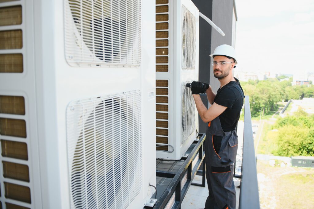 a man wearing a hard hat and gloves working on a large white air conditioner